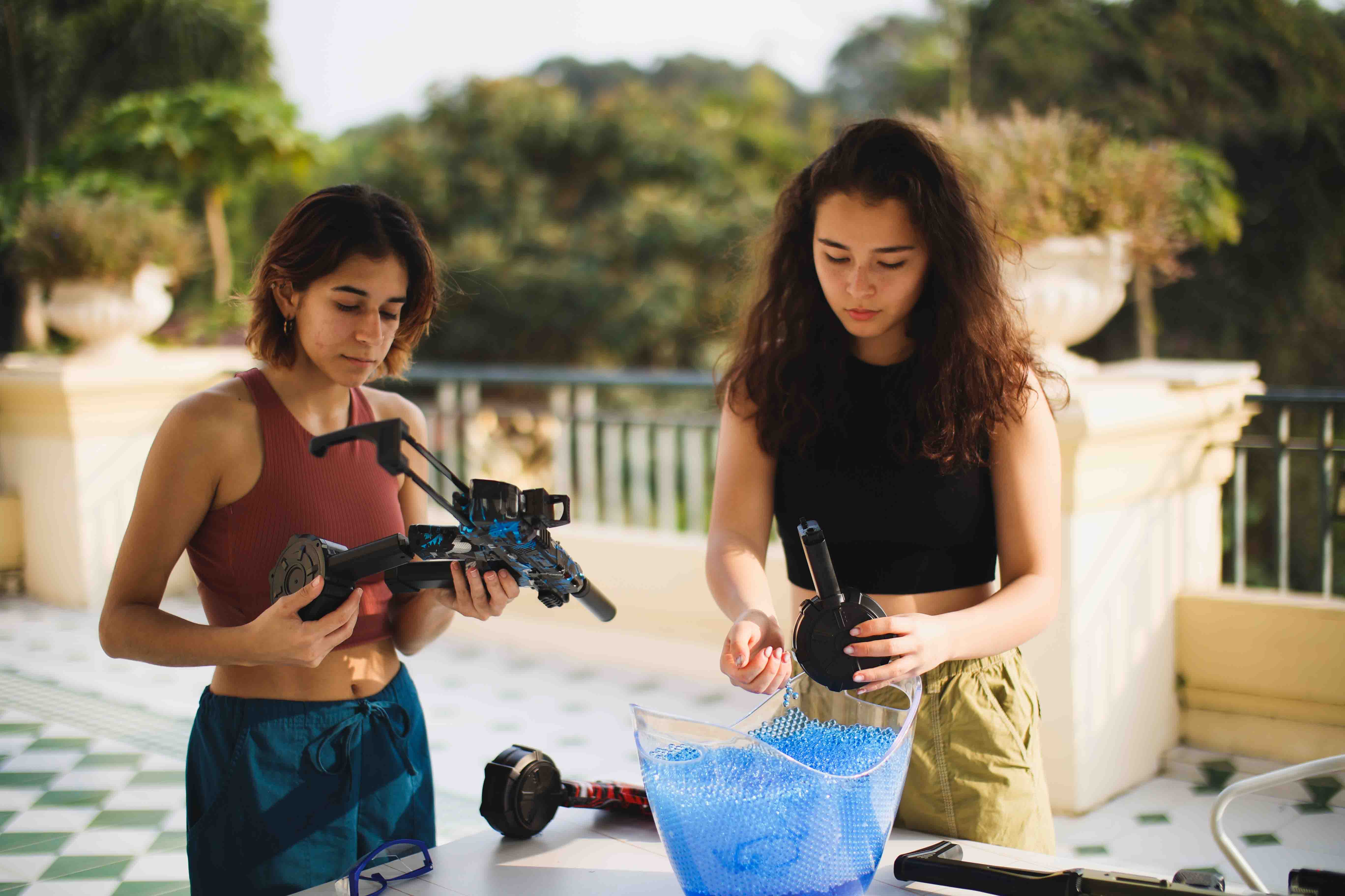 Two women loaded biodegradable blue gel blaster ammunition on a rooftop.