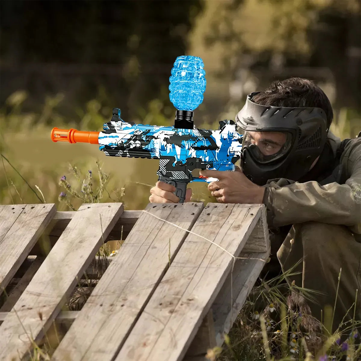 A person outdoors is shooting gel blasting bullets with a blue-black toy gun.