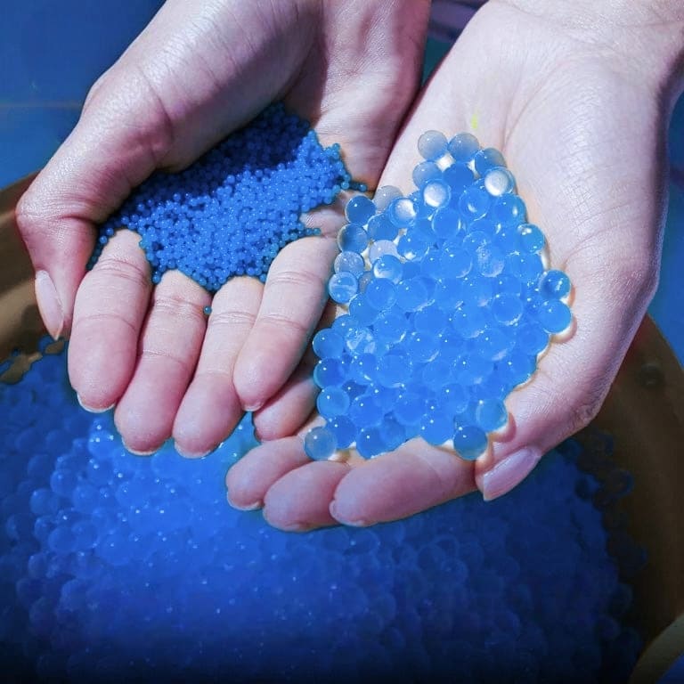 Two hands holding blue gel beads before and after exposure to water, against a blue background.