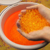 Hand holding orange gel beads above a bucket filled with more gel beads.