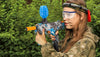 A person holding a blue-gray toy gun using water beads for a gel blaster, against a background of green leaves